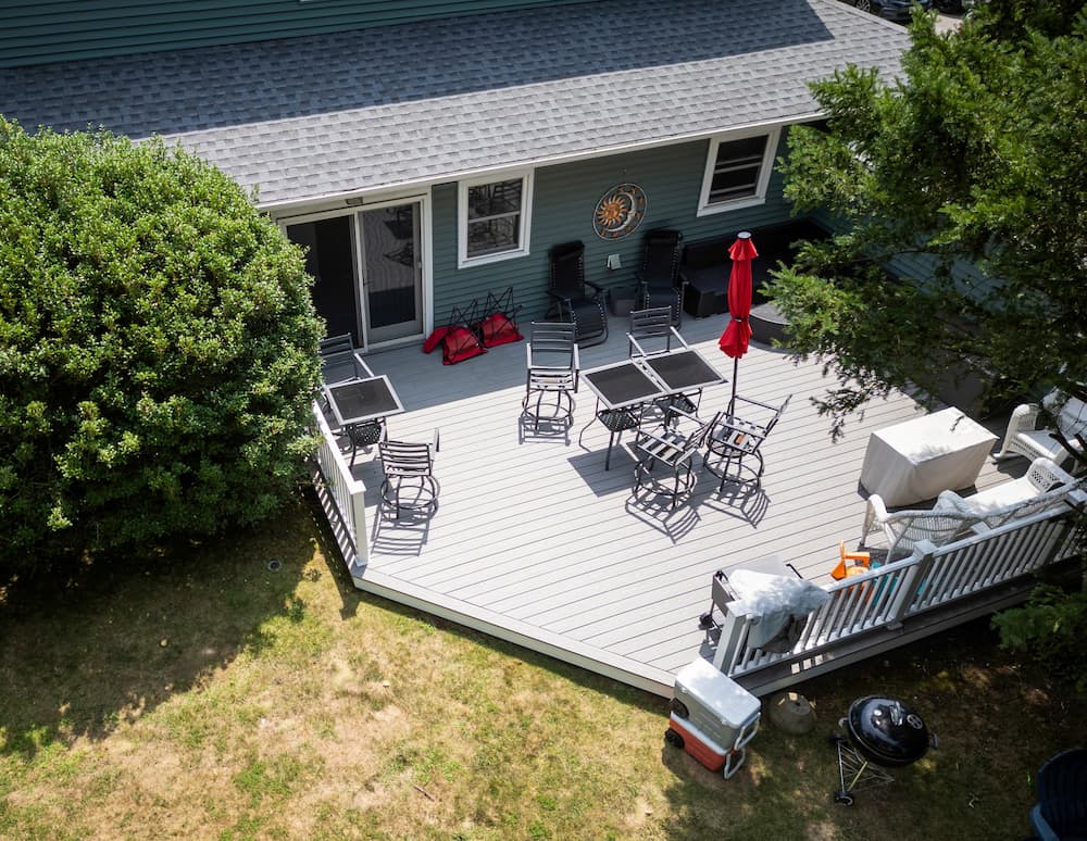 Aerial view of a large grey composite wood deck with outdoor patio furniture and a white railing in a residential backyard.